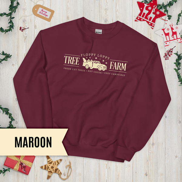 Maroon sweatshirt with 'Floppy Loppy Tree Farm' design on a wooden surface with Christmas decorations.